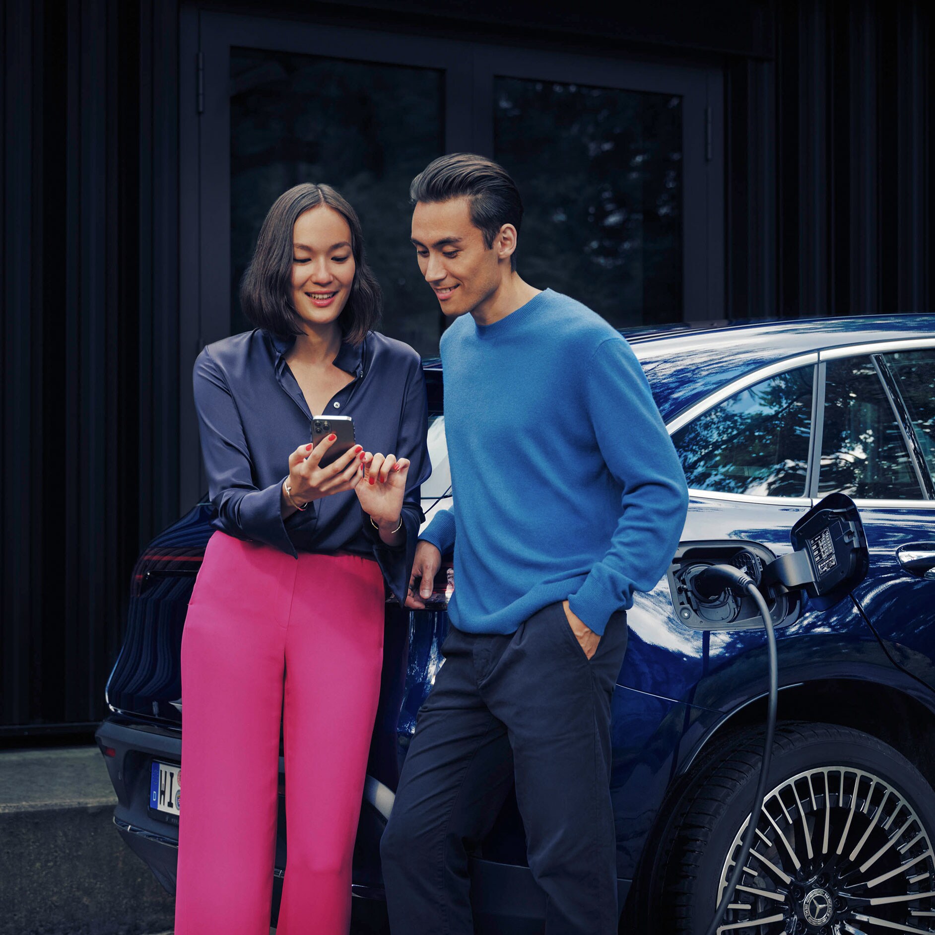 Insurance | Financial | Mercedes-Benz Man and woman looking at a phone together next to blue Mercedes-Benz EQC