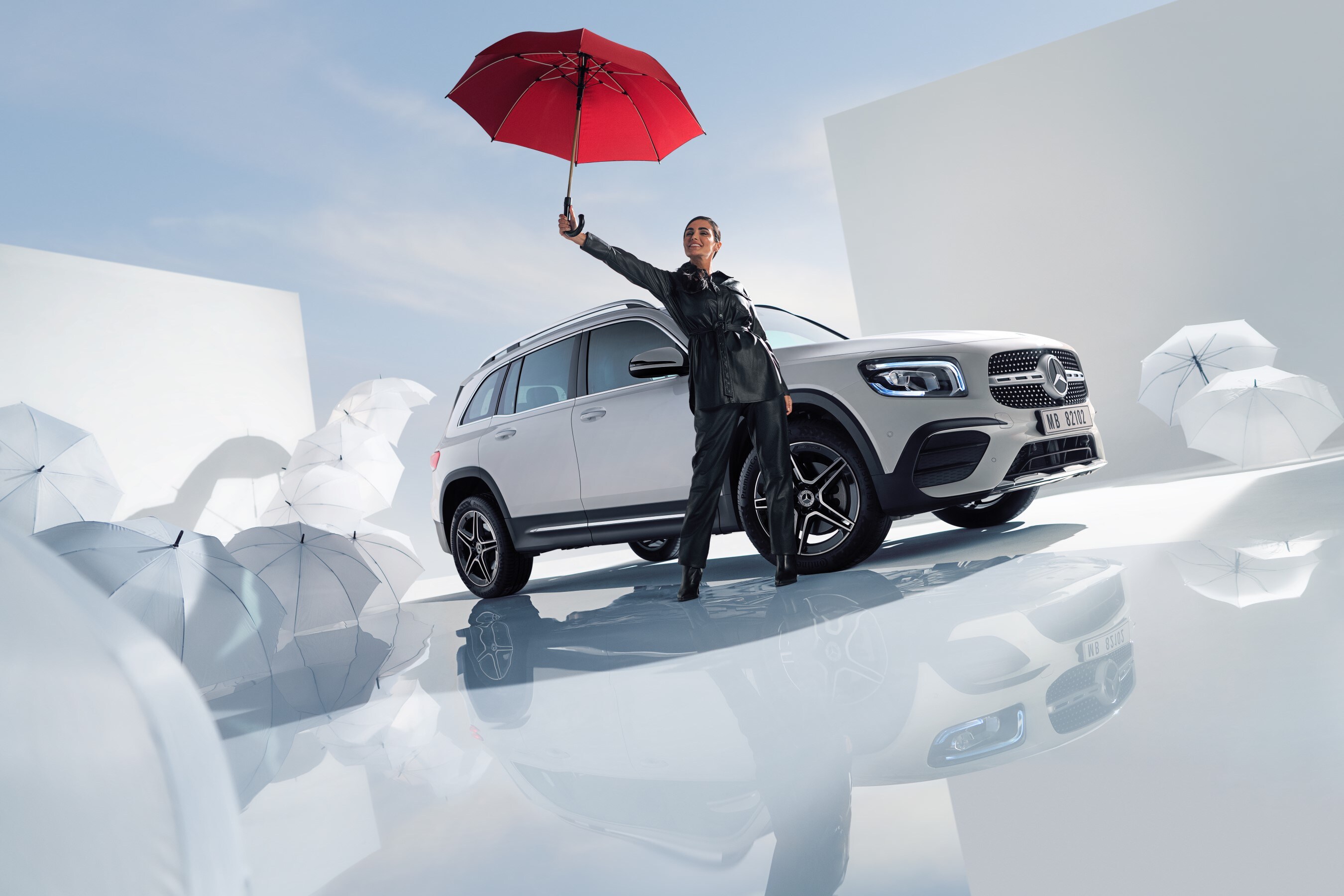 Have a safe journey with the Mercedes-Benz warranty for new vehicles. | Mercedes-Benz A woman is standing beside a Mercedes-Benz with white umbrellas around the floor